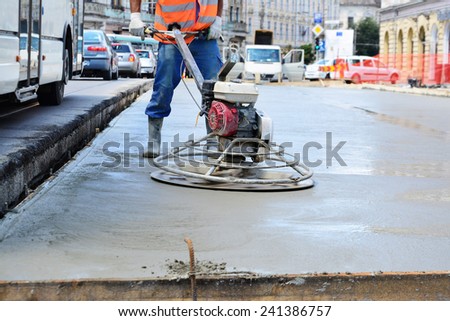 CLUJ-NAPOCA, ROMANIA - CIRCA JULY 2014: Construction worker finishes concrete slab with trowel machine by road upgrade. Road segments are partially closed for traffic on one of the main streets.