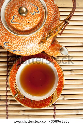 China tea with bubbles in a porcelain cup and saucer and teapot on a mat made of bamboo vertical