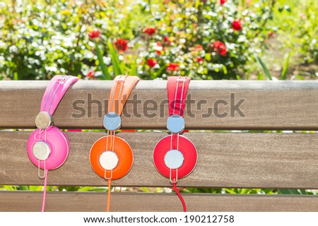 Three varicolored headphones of different colors no wood bench in park
