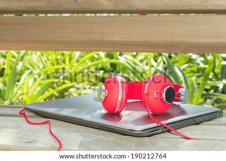 Colorful red headphones and notebook on the wood bench in yard