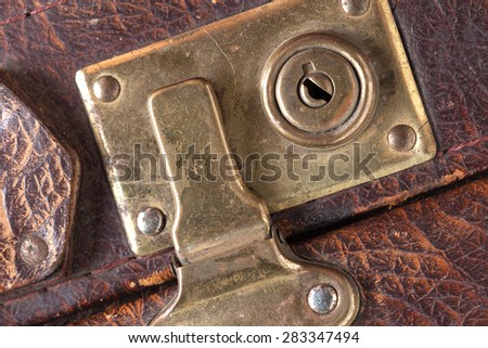 the closed metal rusty lock closeup on part of an old suitcase with the textured leather surface of dark brown color