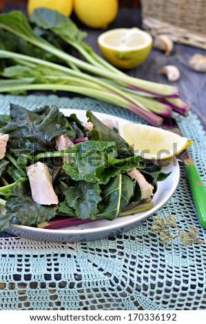 Salad of wild beet leaves with tuna, decoration: a bunch of leaves of wild beets, lemons, garlic, basket with bottles of olive oil.