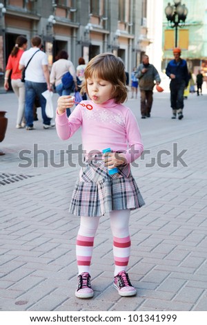 Small girl making soap bubbles in the street