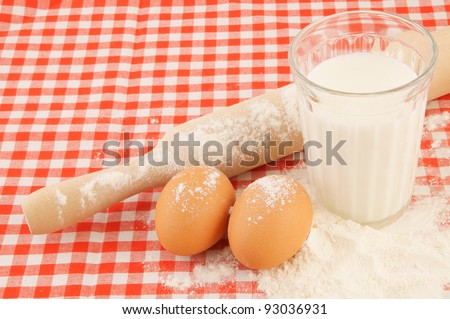 Flour, milk, eggs and rolling pin on red checked tablecloth
