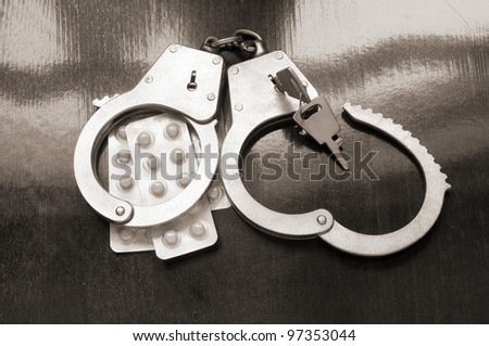 Handcuffs with keys and tablets on wooden background