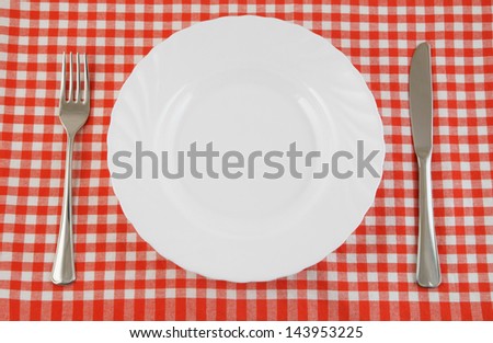 Top view of white plate, fork and knife on tablecloth