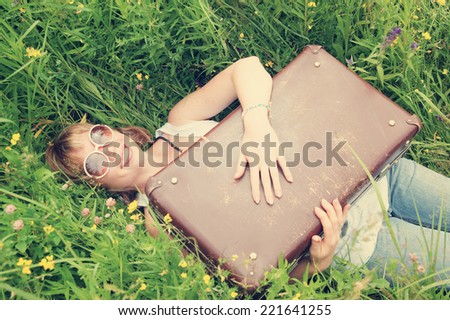 Woman smiling with suitcase in green grass as vacation symbol