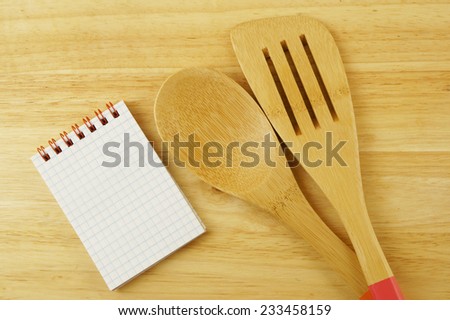 Wooden spoon and spatula with blank notebook on table, receipt concept