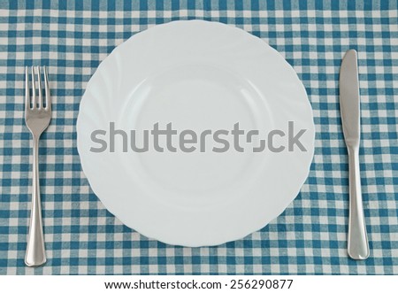 Top view of white plate, fork and knife on tablecloth