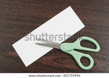 Scissors cutting blank paper card for text on table background