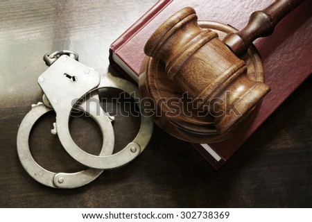 Gavel and handcuffs with red legal book on wooden table