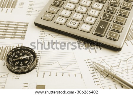 Navigation in financial world concept, pen, calculator and compass on financial charts and graphs