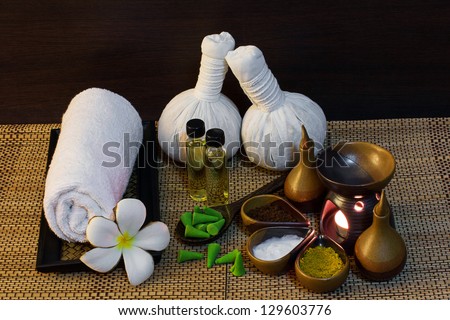 Thai spa massage setting with spa mud,  herbal compress balls, essential oil bottle, towel, frangipani and incense cone