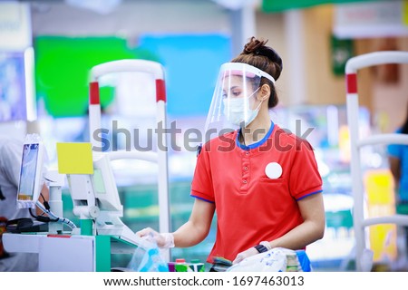 female supermarket cashier in medical protective mask and face shield working at supermarket. covid-19 spreading outbreak  