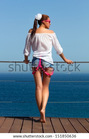 Backside of beautiful woman in denim jeans shorts with pink suspenders