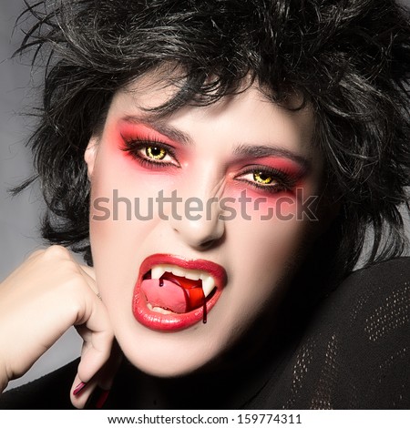 Vampire. Beautiful young woman with fancy makeup, bloody fangs and wolf lenses. Halloween concept