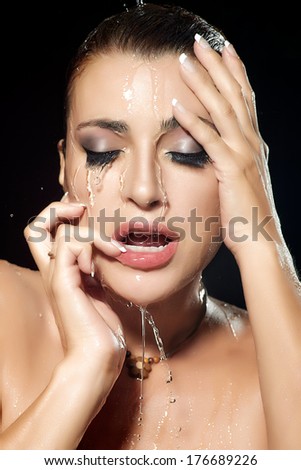 Young woman face with water falling down. Beauty and fashion make-up under flowing water. Closeup portrait isolated on black