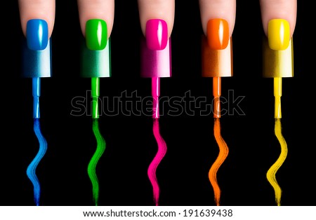 Five fingers with five nail polish brushes painting in fluor colors. Manicure and nail art concept. Closeup image isolated on black