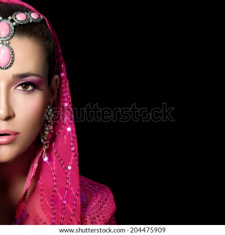 Ethnic beauty. Beautiful hindu woman with traditional clothes, jewelry and makeup covering half face with one hand. Portrait isolated on black