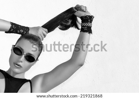 Close up Gorgeous Young Woman in Trendy Fashion, Wearing Black Sexy Clothing and Shades, Pulling her Healthy Long Brown Hair. Monochrome High Fashion Portrait with copy space for text