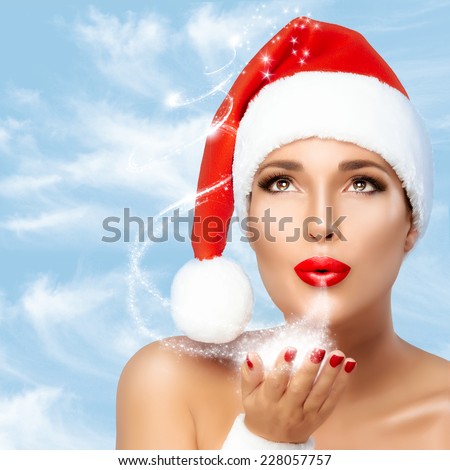 Beautiful Christmas girl in Santa hat blowing star dust. Red lips and manicure. Beauty fashion portrait. Christmas tale concept