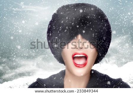 Winter beauty fashion. Joyful face girl gesturing with trendy fur hat covering her eyes on a snowy day. Emotions. High fashion portrait on winter scenery.