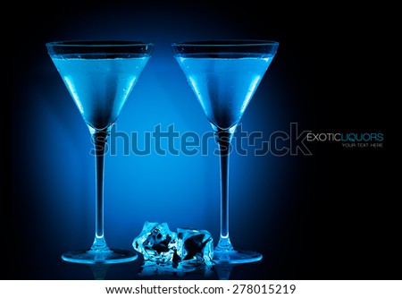 Stemmed cocktail glasses with blue liquor and ice cubes on the table, closeup isolated on black. Template design with sample text