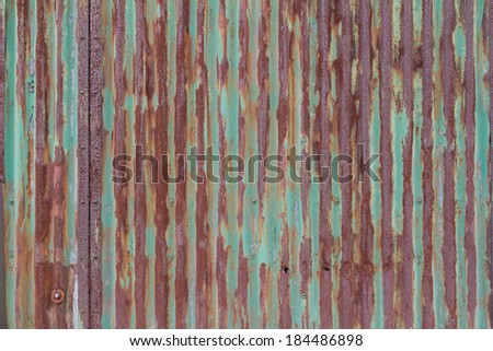 Background texture of rusty corrugated iron cladding on the exterior wall or roof of a building with peeling green paint