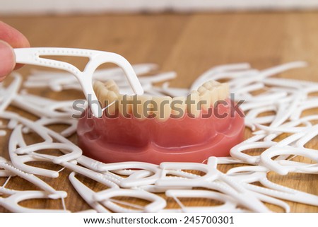 Set of false teeth surrounded by dental floss with a person holding one plastic frame with the floss in position over the teeth for cleaning