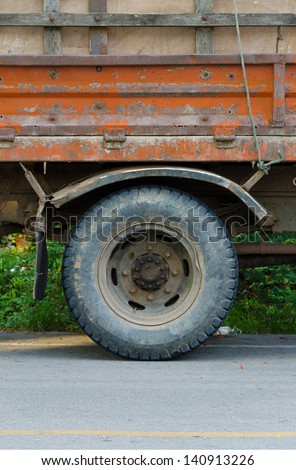 The wheel of the truck is on the road.,Closeup view of a rubber tire on a truck