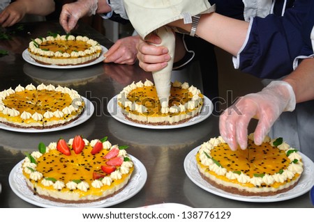 cook placing cream on the top of a passionfruit cheesecake