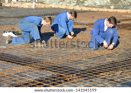 Builders tie off sections of reinforcing for concrete slab foundation of a large building