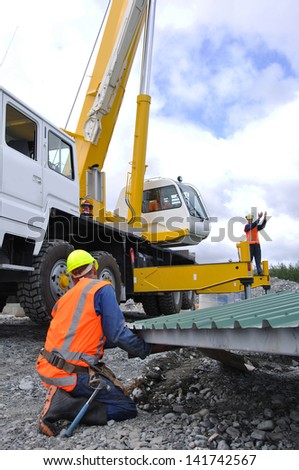 Builder gives directions to crane driver and other men lifting the roof onto a new dairy, Westland, New Zealand