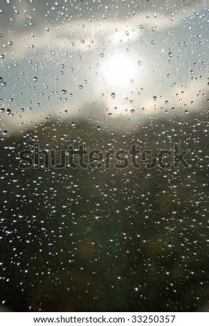 Rain drops on a window glass, with un-sharpen clouds and forest in the background.