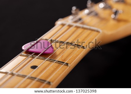 Closeup of a guitar neck with pink pick