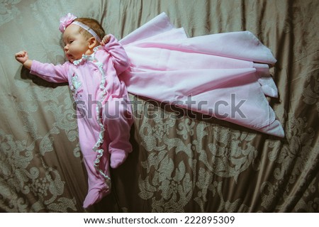 Image of cute little girl in pink suit and cloak indoor. Newborn baby, caucasian child. Super hero in her dreams.