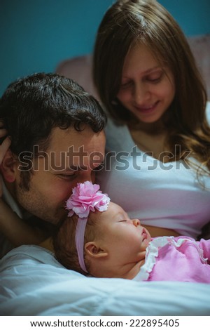 Image of young caucasian family indoor. Father, mother and cute little girl. Dad, mum and newborn baby in pink suit.
