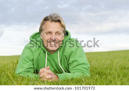 A color portrait photo of a happy smiling blond haired man in his forties laying on the green grass wearing a green colored top.
