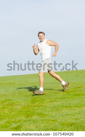 happy smiling man running in a park wearing a white tank top and grey shorts.