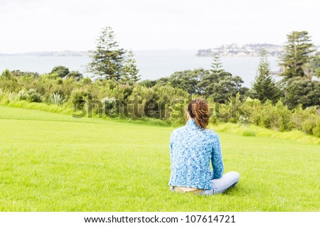 A woman sits alone and feels depressed in a public park overlooking the sea.