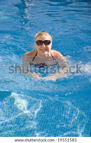 A beautiful older woman in her sixties is enjoying a relaxing swim in the swimming pool during her vacation or retirement in the sun