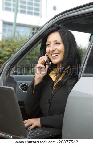 A beautiful indian businesswoman is sitting in her car and enjoying a friendly conversation while working on her laptop computer