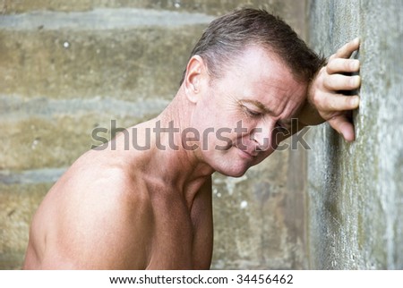 An unhappy and depressed looking man leaning on wall.