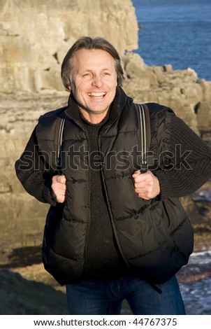 A colour portrait photo of a happy smiling forties man taking a break during a hiking trip along the cliff top.