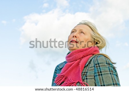 A beautiful older woman in her sixties is looking up to the sky in a thoughtful and contemplative way.