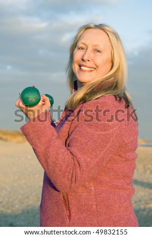 A colour portrait photo of a beautiful older woman in her sixties exercising with dumbells as she smiles at the camera.