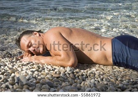 A handsome mature man is sleeping on a pebbly beach