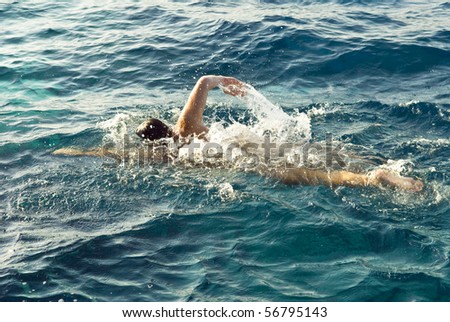 A man swimming front crawl in beautiful blue water.