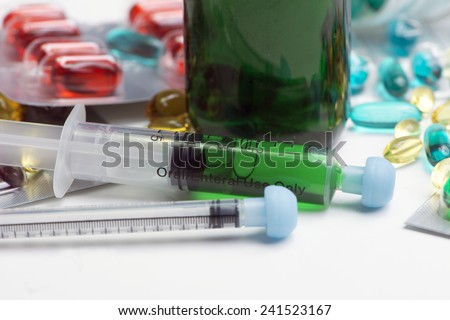 Close-up of green cough medicine bottle with oral syringes and cold remedy capsules.