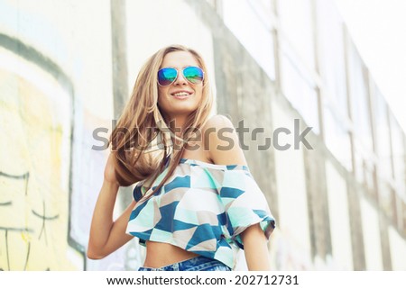 beautiful blond girl in sunglasses standing around the walls with graffiti sunset light